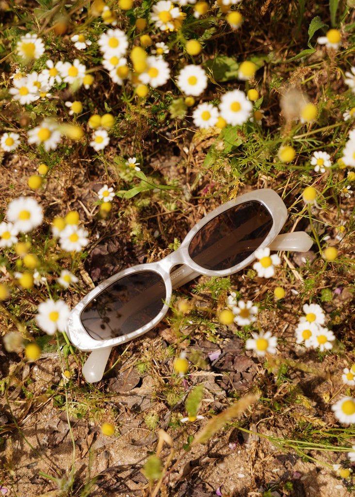Komono EMERY Alabaster Sunglasses — White oval sunglasses with dark lenses laid on grass — MYFASHIONFRUIT