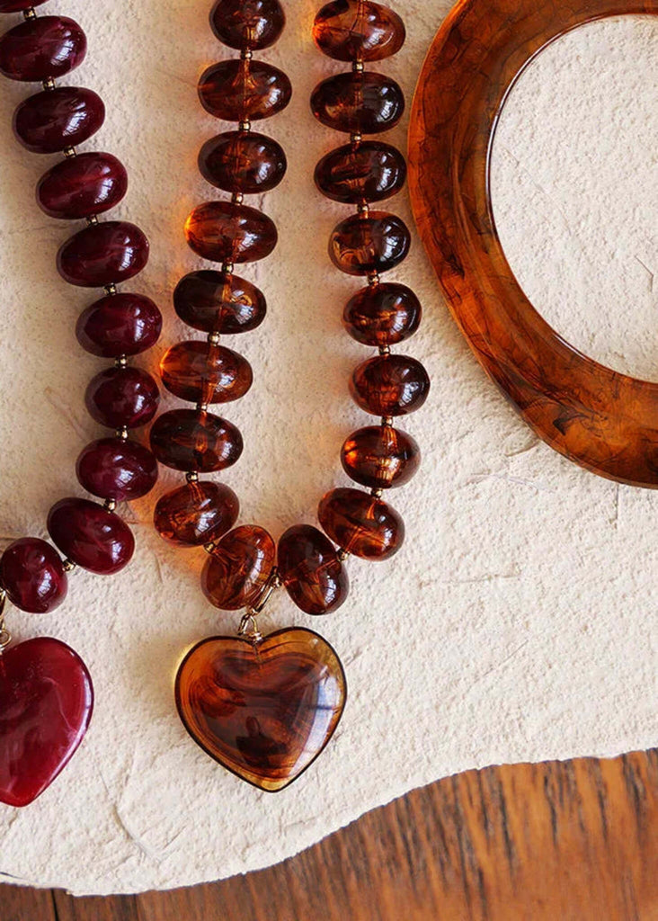Two necklaces with heart pendants and a tortoiseshell bracelet on a textured surface.