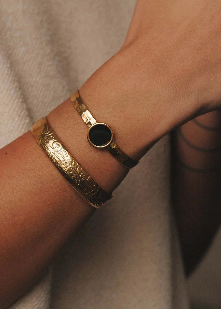 Treasure Cuff — Two gold cuffs on model's wrist, one with floral detail, one with black stone — MYFASHIONFRUIT